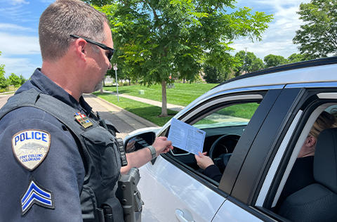 Police offer takes blue envelope from person in parked car.