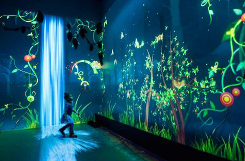 small child looks at bright glowing lights on dark museum room