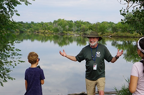 City of Fort Collins Natural Areas volunteer smiling brightly as he holds his hands wide open and instructs community members about the Natural Area they're in.
