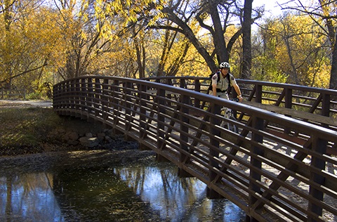 Ranger riding cyclist over bridge crossing Poudre River at Salyer Natural Area.