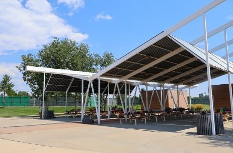 A sheltered pavilion with picnic tables and grills on the edge of a park