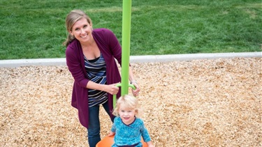 A woman pushes a young girl on a swing