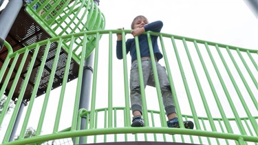 A young boy peeks over the railing on a playground structure