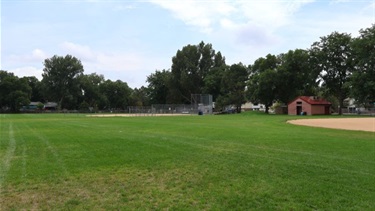A large grassy field near two ball fields