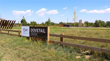 A Dovetail Park sign on a fence in front of a park