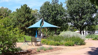A covered park pavilion next to a pollinator garden and sidewalk