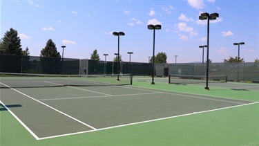 A tennis court with lights on a sunny day