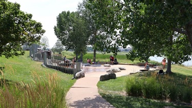 A splash pad area surrounded by trees next to a lake