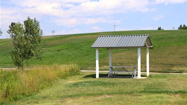 A small shelter with a picnic table in front of a grassy hill