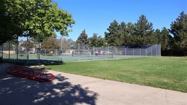 Tennis courts in a park shaded by trees