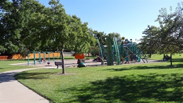 A park playground surrounded by trees and paved paths