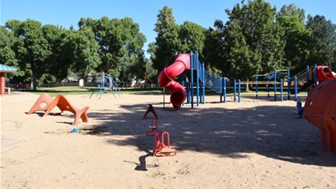 A sand-filled playground with a slide, swing set and other play structures
