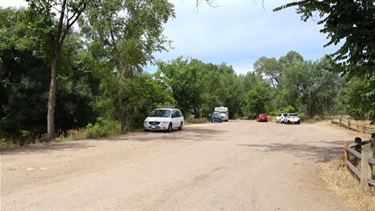 A dirt parking lot with a few cars surrounded by trees