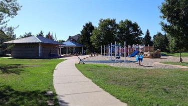 A paved path leading to a park playground and shelter buildings