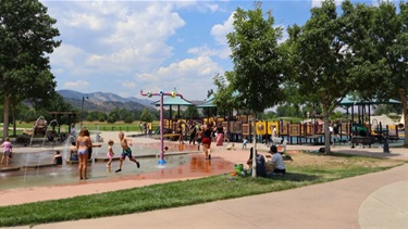 Kids play on a splash pad next to a playground at a park