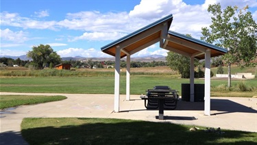 A small covered shelter with a picnic table and grill at a park