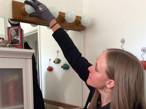 Person wearing gloves replacing a light bulb above a bathroom mirror.