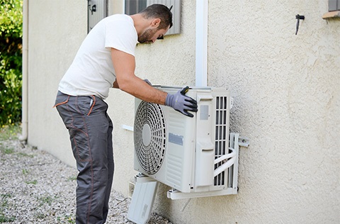 A person installing a heat pump on the side of a house