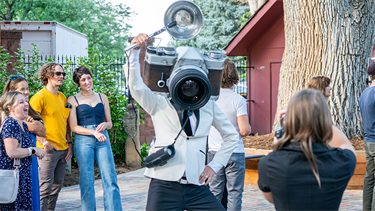 person in giant camera head costume among crowd