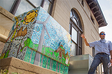 Person gestures at mural on transformer cabinet.