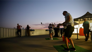 person swings golf club on rooftop at dusk