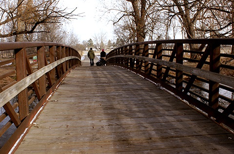 Two people walking across a bridge over a river.