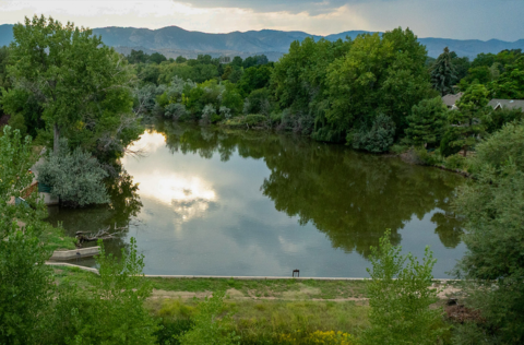 A large pond in the evening, with the reflection of nearby trees on the water's surface and mountains in the background.